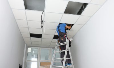 Installing ceiling lighting. Electrician working on step ladder in room